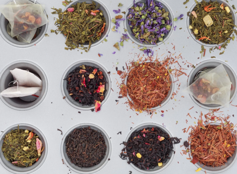 Create a collage featuring images of classic black tea leaves, green tea leaves, white tea leaves, oolong tea leaves, and herbal ingredients used in Harney & Sons teas. Featured images