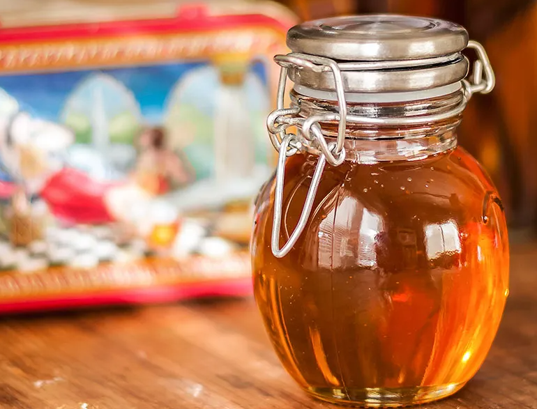 Jar of honey infused with white clover, with a drizzle over a teaspoon.